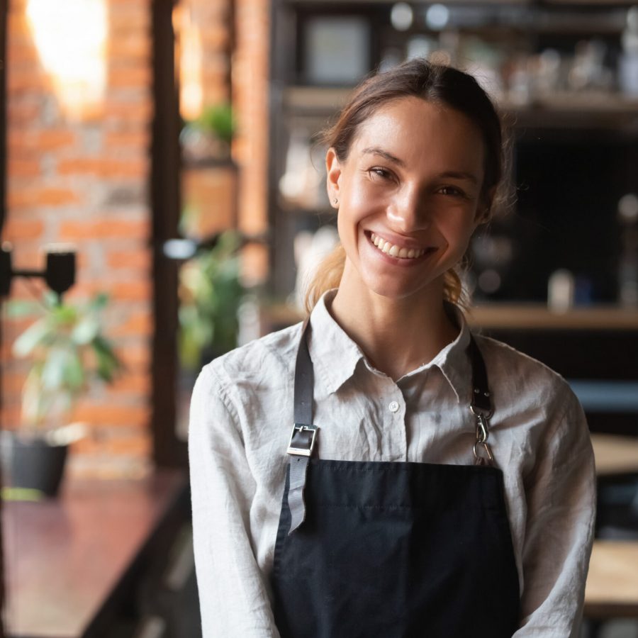 Head shot portrait successful mixed race businesswoman happy restaurant or cafeteria owner looking at camera, woman wearing apron smiling welcoming guests having prosperous catering business concept