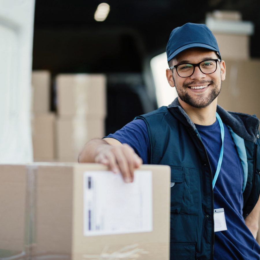 Portrait of happy worker unloading boxes from a delivery van and looking at camera.